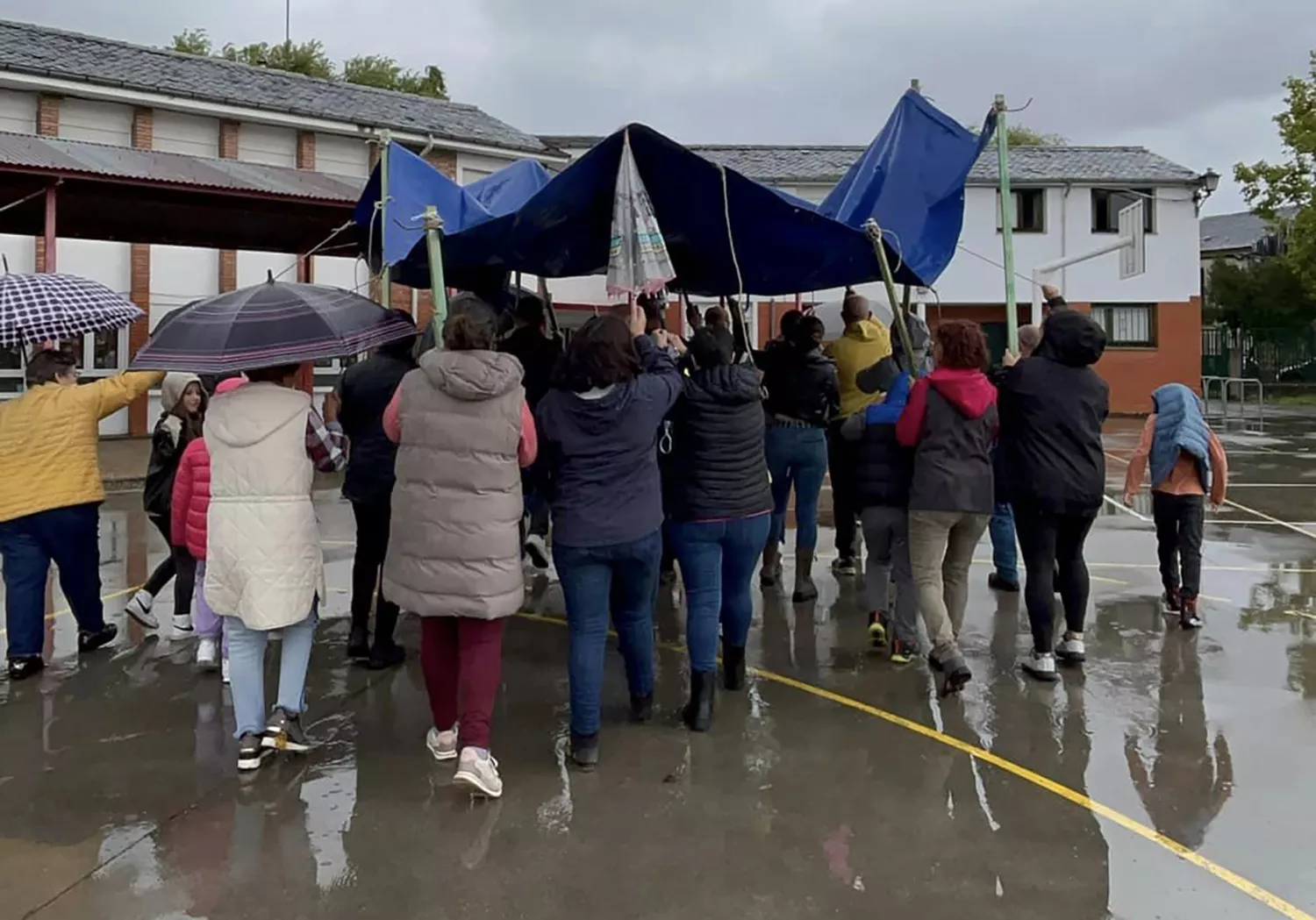 Una lona sirve de techo móvil a los niños del colegio de Columbrianos para disfrutar del recreo a pesar de la lluvia